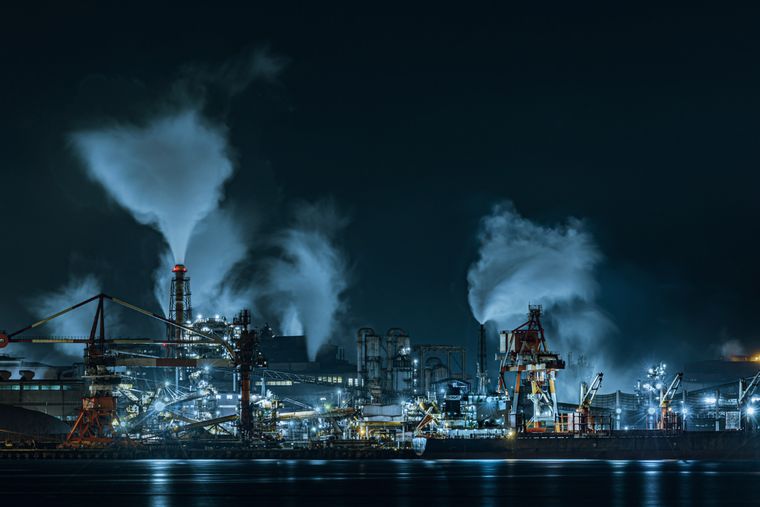 Site industriel de nuit, panaches de vapeur au-dessus des installations